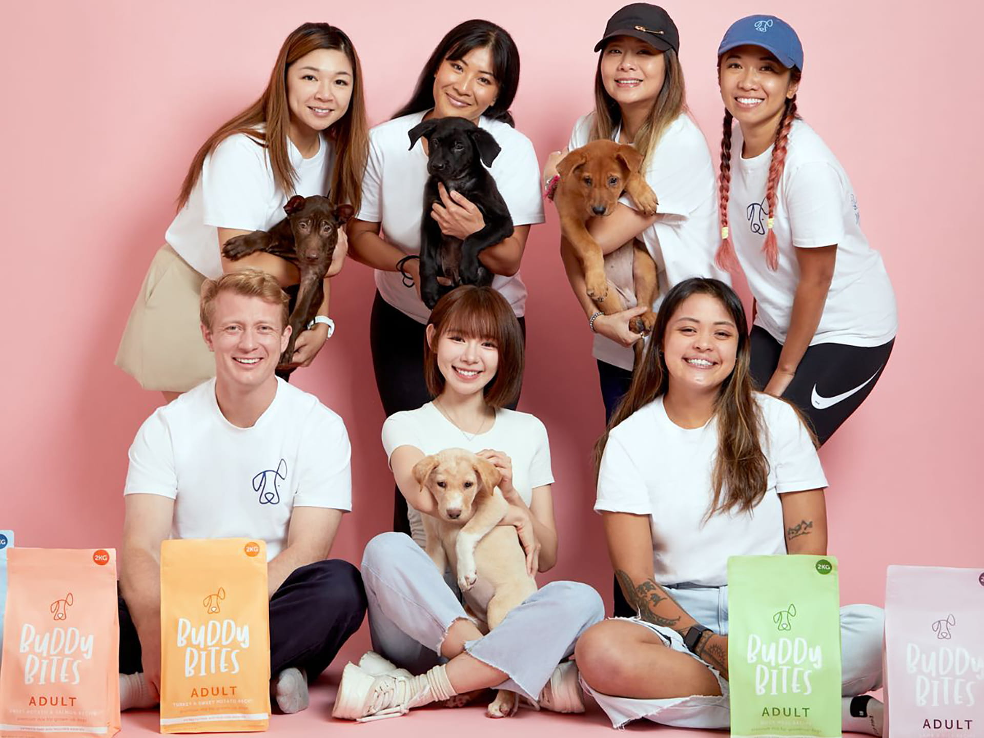 Buddy Bites' team including Malaysian actress Lin Mei Chen with rescue puppies and Buddy Bites branded pet food packaging.