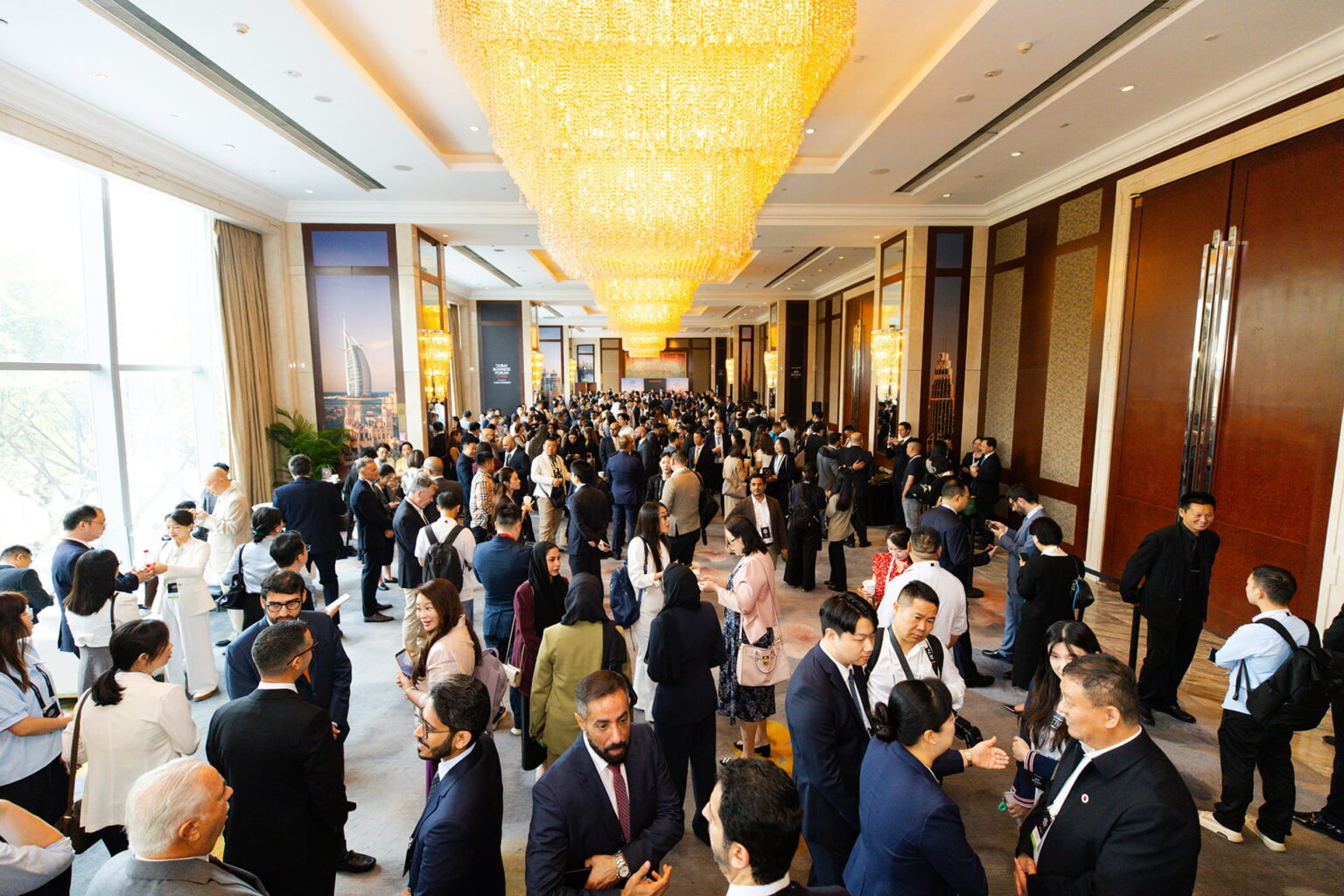 Hundreds of delegates in business attire networking beneath a large crystal chandelier in a Shenzhen hotel ballroom.