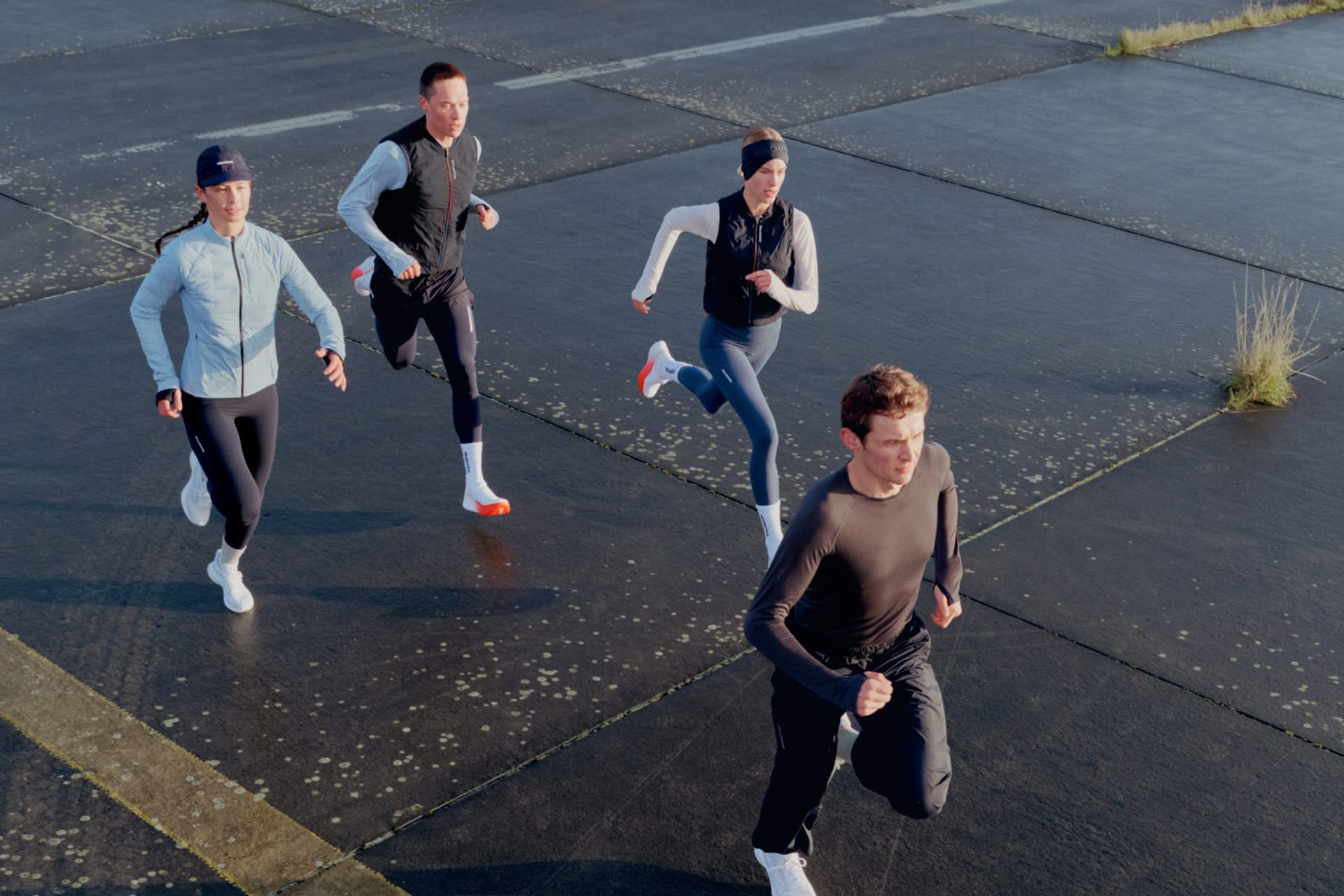 Four runners in Salomon's Falcon Fly technical apparel on a wet runway at dawn.